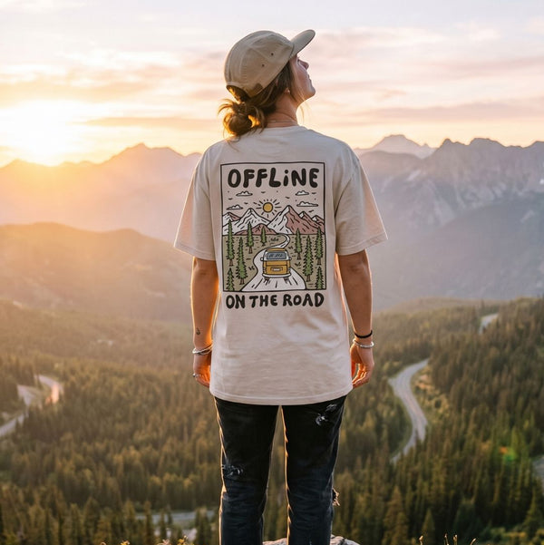 Person wearing a t-shirt with 'Offline on the Road' design, standing in a mountainous landscape at sunset.