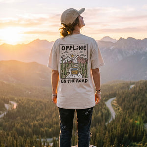 Person wearing a t-shirt with 'Offline on the Road' design, standing in a mountainous landscape at sunset.