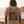 A man viewed from behind wearing a beige t-shirt with a large graphic print of palm trees, mountains, and ocean waves on the back, set against a coastal sunset background.