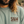 Close-up of a person wearing a sage green crewneck sweatshirt with a brown 'S&W CLOTHING' logo printed on the chest.